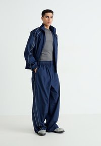 Navy windbreaker and loose pants made of lightweight fabric, featuring contrasting white stitching and an elastic waistband.