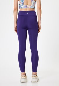 Paarse leggings met een hoge tailleband, een gladde textuur en een aansluitend ontwerp, gecombineerd met witte sportschoenen.