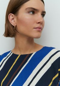 Robe rayée bleue et blanche avec des rayures diagonales noires et marron. Manches courtes et encolure large. Accessoire en créoles dorées.