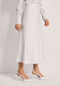 Woman wearing a high-waisted, white midi skirt with a matching white long-sleeve blouse and white slingback heels with a pointed toe.