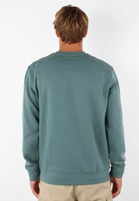Sweatshirt vert avec un col rond, des poignets et un ourlet côtelés, une texture douce et un petit logo sur l'épaule.