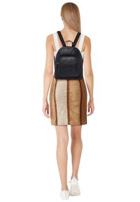Black leather backpack with a rounded shape, front zip pocket, and adjustable straps. Paired with a brown and beige patterned skirt.