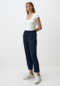 Marine joggerbroeken met elastische tailleband en trekkoorddetail; gecombineerd met een aansluitend wit T-shirt met korte mouwen en witte sneakers.