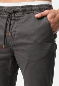 Pantalones de algodón grises con cinturilla elástica, cordón y puntas de acento naranjas. Cuentan con bolsillos laterales y una textura suave.