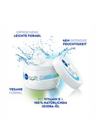 White round jar of Nivea Soft cream with a clear lid, featuring blue and green accents. Texture appears creamy, with water droplets around it.