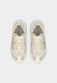 Ζευγάρι μπεζ και λευκά αθλητικά παπούτσια Calvin Klein με κορδόνια, σε θέα από πάνω σε απλό λευκό φόντο.