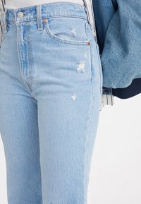 Vaqueros de mezclilla azul claro con una cintura alta, detalles ligeramente desgastados y pierna recta. Presenta herrajes de cobre y una textura suave.