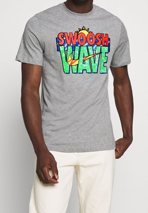 Graues Baumwoll-T-Shirt mit mehrfarbigem "SWOOSH WAVE"-Textdesign und Nike-Logo, kurzen Ärmeln und Rundhalsausschnitt.