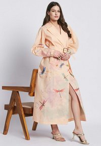 Abito color pesca con vita accentuata da una cintura, maniche lunghe e uno spacco alto, impreziosito da motivi di libellule e spruzzi di colori pastello.