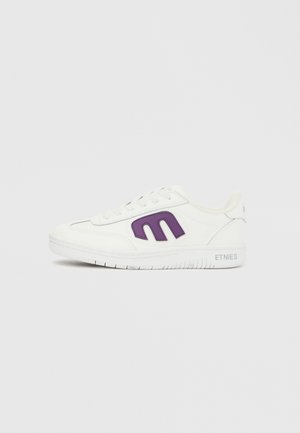 Bijela niska tenisica s ljubičastim logotipom "Etnies" na boku, bijelim vezicama i natpisom "Etnies" na srednjem đonu blizu pete.