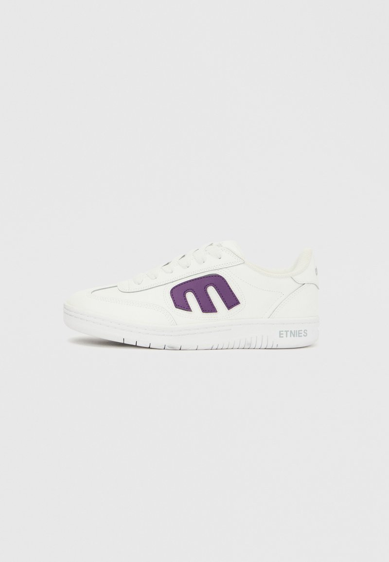 Baskets basses blanches avec logo "Etnies" violet sur le côté, lacets blancs et texte "Etnies" sur la semelle intermédiaire près du talon.