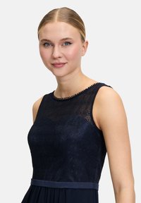 Granatowa sukienka z koronkowym górnym krojem i prostym dekoltem, z gładką talią i warstwową spódnicą, podkreślająca skomplikowane wzory.