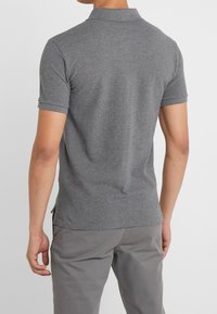 Grå polo med korta ärmar och krage, med en enfärgad struktur och sidslitsar vid fållen för ökad rörelsefrihet.