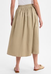 Knielanger, beiger Baumwollrock mit elastischem Bund und gerafften Falten. Glatte Textur und einfarbig ohne sichtbare Muster.