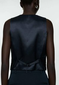 Schwarzes ärmelloses Top aus Satin mit glatter Textur, Rückenknotendetail und einem klaren, minimalistischen Design.