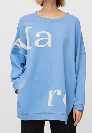 Sweatshirt surdimensionné bleu clair en tissu doux, avec un grand texte blanc et un col rond. Poches sur les côtés et coupe décontractée.
