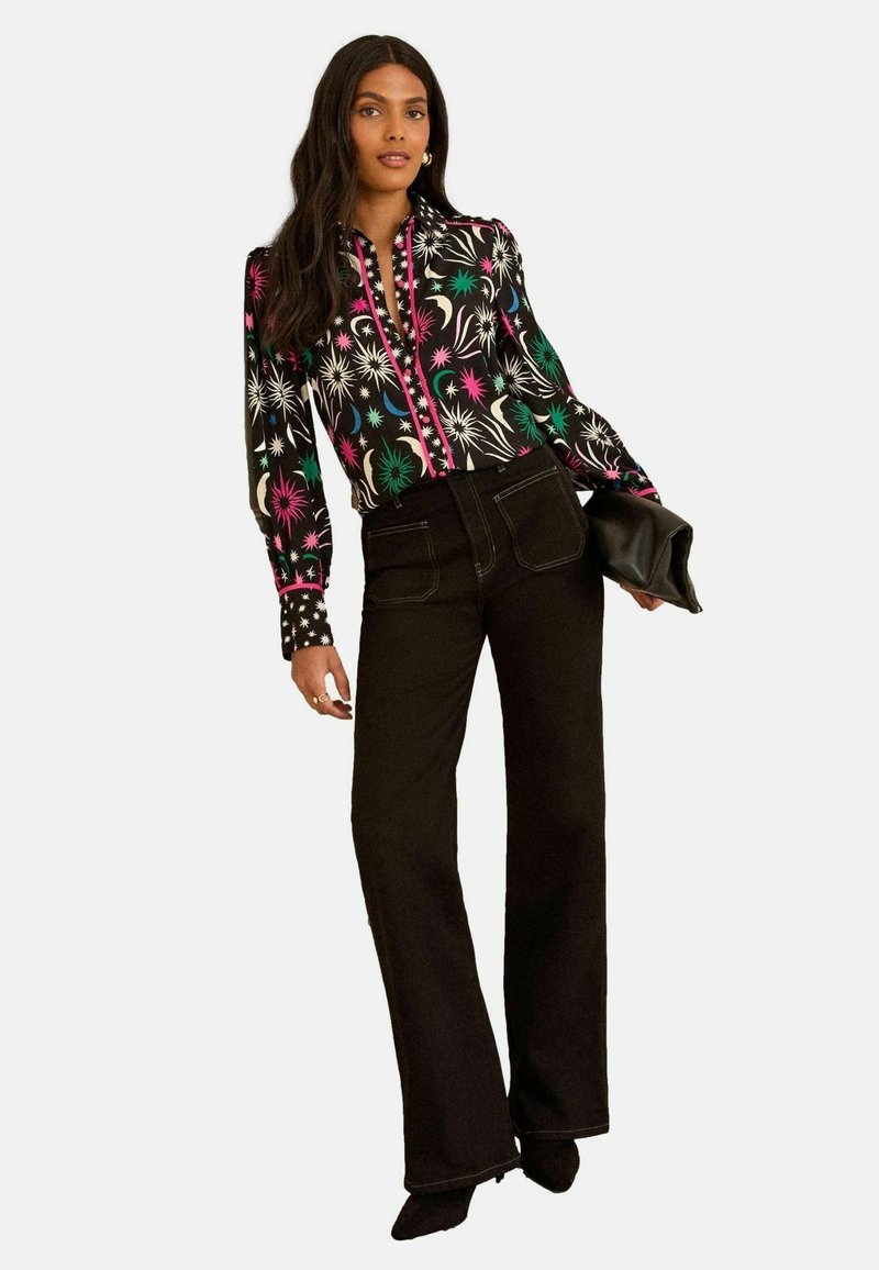 Långärmad blus i svart, med färgglada blommönster, knapp-up front och kontrasterande prickiga ärmslut. I kombination med svarta utsvängda byxor.