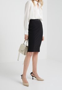 Vit blus med knappar, svart pennkjol, beiga högklackade skor med svarta detaljer, och en ljusgrå handväska med repremmar.