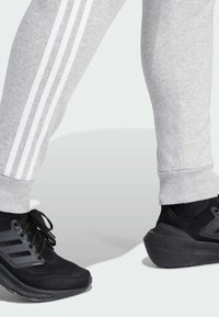 Grijze joggingbroek met witte zijkanten, gecombineerd met zwarte sportschoenen met een gestructureerd lijf en een opvallend loopvlakdesign.
