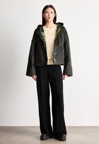 Lühendatud must kapuutsiga jakk kollaste paeltega, kantud beežist pealsele; kombineeritud laiade mustade pükste ja massiivsete mustade kingadega.