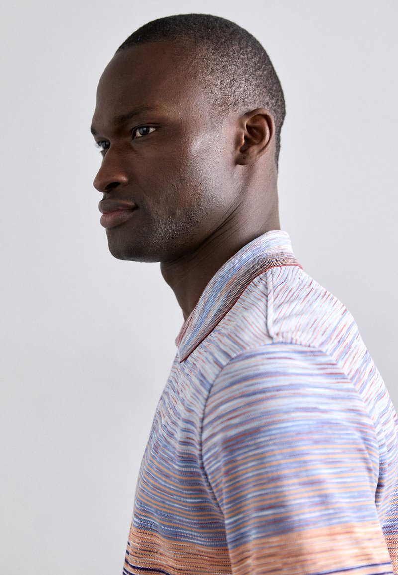 Gestreiftes Poloshirt mit horizontalen Linien in Blau, Orange und Weiß. Mit einem Kragen und kontrastierenden Detailverzierungen.