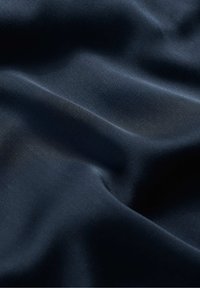 Laavansininen kangas, jossa on sileä, pehmeä pinta ja hienovarainen kiilto. Materiaali näyttää kevyeltä ja laskeutuu lempeästi virtaavilla taitoksilla.