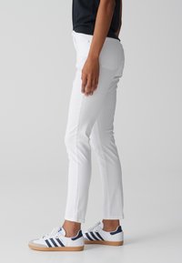 Jeans blancos ajustados con una textura suave, diseño de cinco bolsillos y detalles de costura sutiles, combinados con zapatillas blancas con acentos en azul marino.