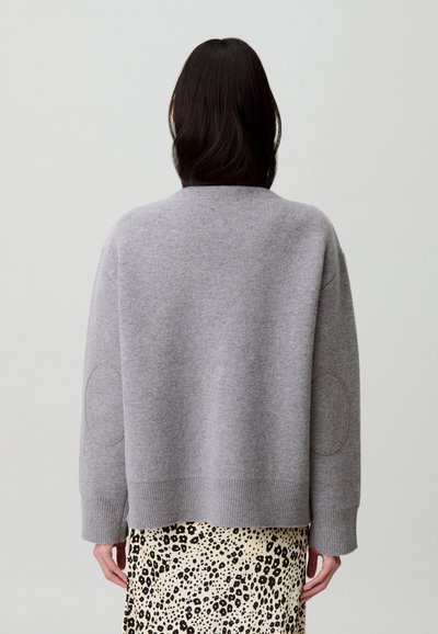 Jersey gris de ajuste relajado, dobladillo acanalado y hombros estilo silla de montar. Presenta parches en los codos y está combinado con una falda de estampado de leopardo.