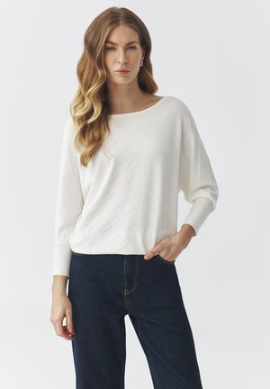 Witte, lange mouwen top met een chevronstructuur, ronde hals en een ontspannen pasvorm, gecombineerd met donkere denim jeans.