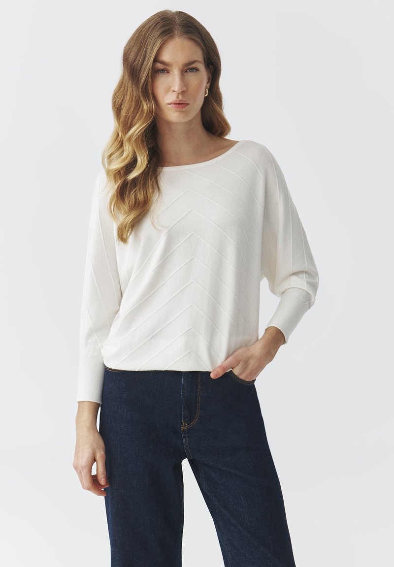 Hvid, langærmet top med chevron-struktur, rund halsudskæring og afslappet pasform, parret med mørk denim jeans.