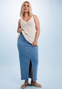 Neulotusta kermaista tanktopista, jossa on pystysuunnassa raidat, on yhdistetty korkeavyötäröiseen farkuhameeseen, jossa on sivuaukko, sekä kultaisiin sandaaleihin.