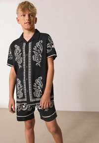 Čierny set s krátkymi rukávmi a šortkami, zdobený bielymi paisley a kvetinovými vzormi, s golierom a zapínaním na gombíky vpredu.