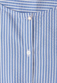 Chemise rayée verticalement bleu et blanc, gros plan de l'avant avec deux boutons, un rond en métal et un blanc en plastique, visibles près du col.