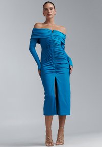 Robe bleue épaules dénudées avec manches longues, texture froncée, fente à l'avant et petit détail métallique au niveau de l'encolure.