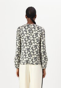 Langarmbluse mit schwarzem Hintergrund und weißem Blumenmuster. Verfügt über einen runden Ausschnitt und einen geraden Schnitt, aus leichtem Stoff gefertigt.