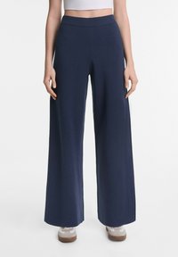 Weite Hosen aus navyblauem Stoff mit einem gerippten Bund. Sie haben eine glatte Textur und fallen gerade von den Hüften bis zum Boden.