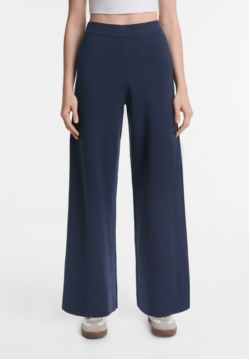 Weite Hosen aus navyblauem Stoff mit einem gerippten Bund. Sie haben eine glatte Textur und fallen gerade von den Hüften bis zum Boden.