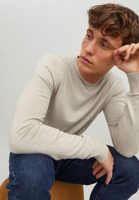Light beige long-sleeve sweater with a crew neckline, fitted design, and ribbed cuffs, paired with dark blue jeans.