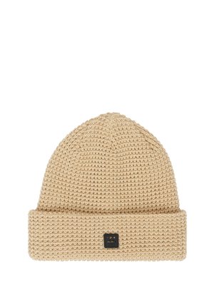 Beige gestrickte Wollmütze mit umgeschlagenem Bündchen und einem kleinen schwarzen quadratischen Logo-Patch auf der Vorderseite in der Mitte.