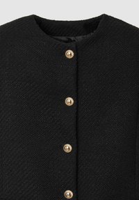 Cappotto nero strutturato con scollatura rotonda, caratterizzato da bottoni dorati che decorano tutta la parte anteriore. Il tessuto appare spesso e caldo.