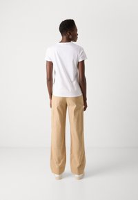 White short-sleeve t-shirt with a rounded neckline, paired with beige wide-leg pants featuring side pockets. Tailored fit, smooth texture.
