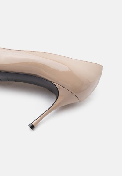 Μπεζ γυαλιστερό δερμάτινο γοβάκι στιλέτο με μυτερή μύτη και λεπτή μαύρη άκρη τακουνιού σε λευκό φόντο.