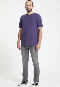 T-shirt en coton violet avec un col rond, associé à un jean gris clair et des baskets noires. Aucune motif ou accent visible.