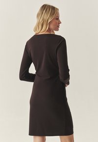 Vestido negro de manga larga hecho de tejido suave, con escote redondo y una silueta ajustada, alcanzando la longitud a mitad del muslo.