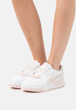 Zapatillas blancas con acentos rosas, materiales de cuero y ante, puntera redonda, suela plana y logo de marca prominente en el lateral.