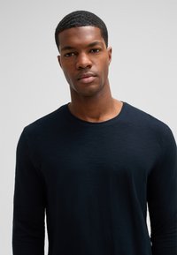 Langärmliges dunkelblaues Hemd mit Rundhalsausschnitt, aus einem weichen, strukturierten Stoff, mit einer figurschmeichelnden Silhouette. Keine Muster oder Akzente.