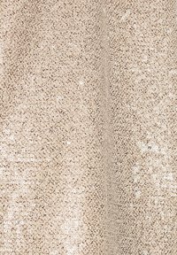Tissu tricoté beige avec de petites paillettes brillantes couvrant uniformément la surface, créant un motif texturé et légèrement réfléchissant.