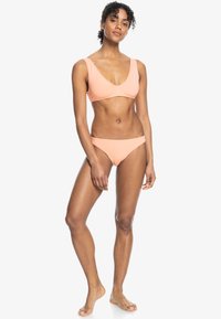 Licht perzik bikini set met een scoop halstoop en brede banden, en een low-rise onderstuk. Gladde textuur en minimalistisch ontwerp.