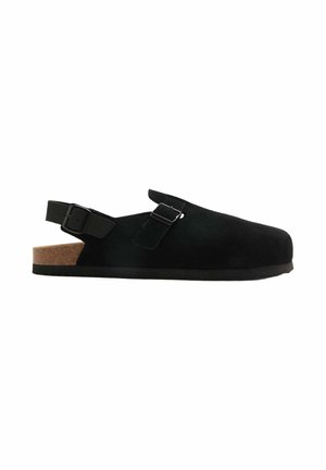 Sort ruskind slip-on sandal med to justerbare spænder og korkfodbed, flad sål og åben hælrem.