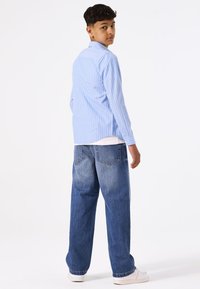Camisa a rayas azul clara con mangas largas, combinada con jeans azules de corte holgado y zapatillas blancas. Diseño sencillo y casual.